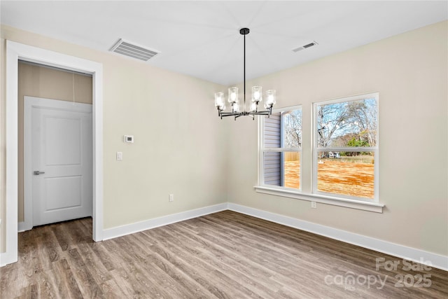 unfurnished dining area with a notable chandelier, wood finished floors, visible vents, and baseboards