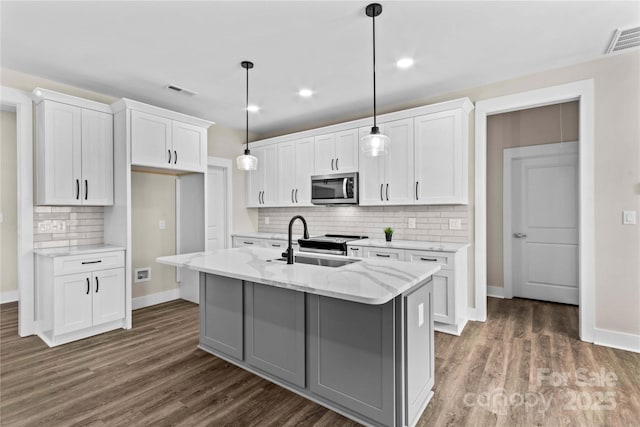 kitchen featuring a sink, stainless steel microwave, visible vents, and dark wood-style floors