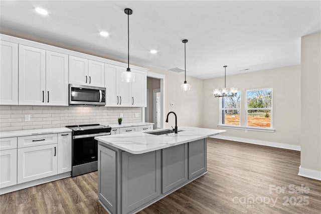 kitchen featuring a center island with sink, a sink, stainless steel appliances, dark wood-type flooring, and backsplash