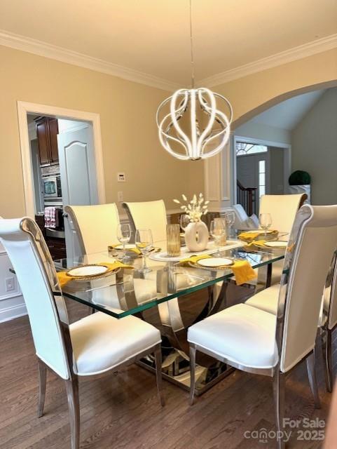 dining room with a notable chandelier, arched walkways, dark wood-type flooring, and ornamental molding