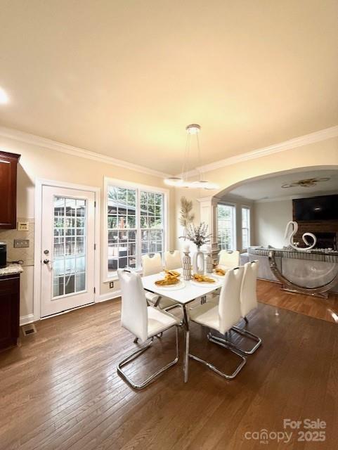 dining room with a wealth of natural light, wood-type flooring, arched walkways, and crown molding