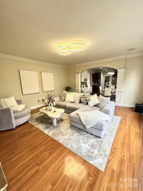 living room with baseboards, arched walkways, light wood-style flooring, and ornamental molding