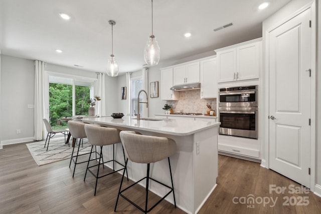 1439 Hubert Graham Way, Tega Cay, SC 29708 - kitchen with a sink, double oven, backsplash, an island with sink, and dark wood-style floors
