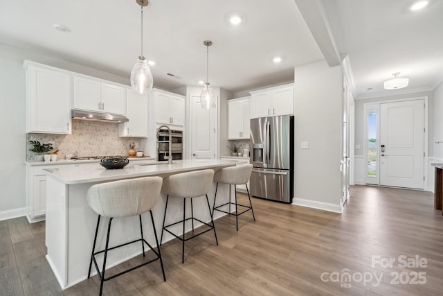 1439 Hubert Graham Way, Tega Cay, SC 29708 - kitchen featuring appliances with stainless steel finishes, under cabinet range hood, recessed lighting, tasteful backsplash, and a breakfast bar