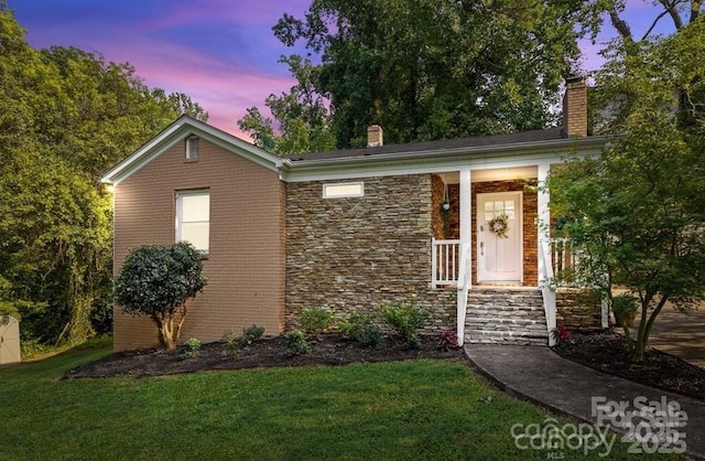 view of front of property with stone siding, a lawn, and a chimney