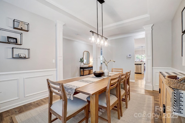 dining space featuring crown molding, light wood-style flooring, and ornate columns
