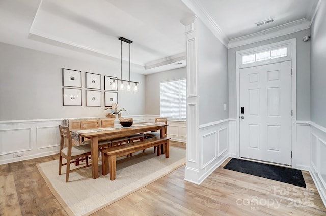 entryway with a tray ceiling, ornamental molding, a decorative wall, and visible vents