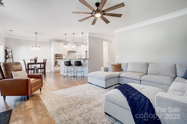 living area with visible vents, ornamental molding, light wood-style floors, baseboards, and ceiling fan with notable chandelier