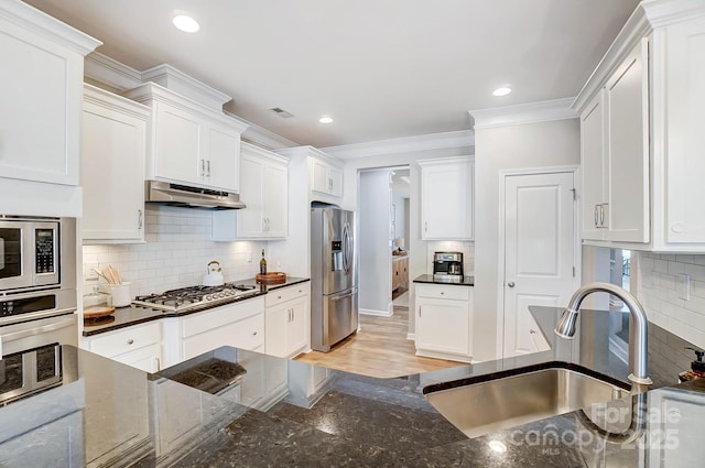 kitchen with under cabinet range hood, ornamental molding, a sink, white cabinetry, and appliances with stainless steel finishes