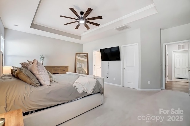 bedroom with a tray ceiling, carpet flooring, visible vents, and baseboards