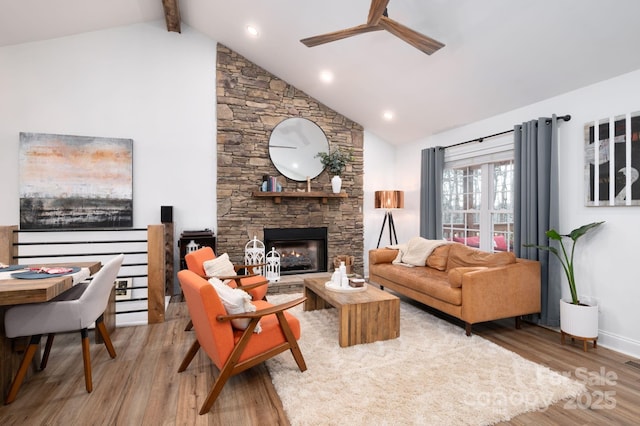 living area with beamed ceiling, light wood-style floors, a stone fireplace, and a ceiling fan