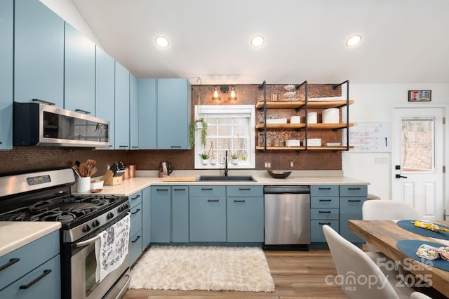 kitchen with light countertops, light wood-style flooring, appliances with stainless steel finishes, blue cabinets, and a sink