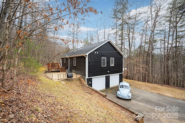 view of side of home with aphalt driveway, a wooden deck, and an attached garage