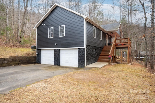 view of property exterior featuring stone siding, an attached garage, stairs, and driveway