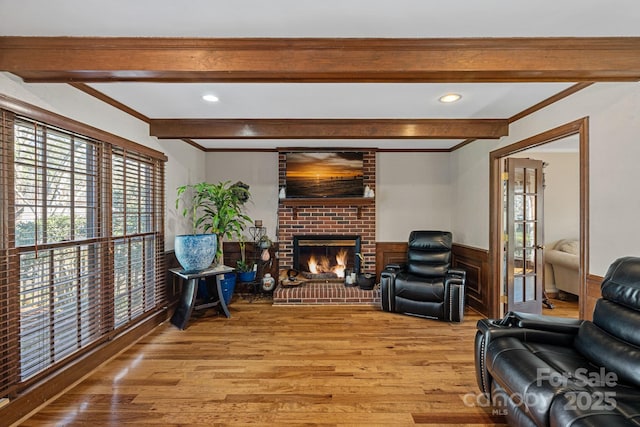 living room with beamed ceiling, light wood-style floors, a wainscoted wall, and a fireplace