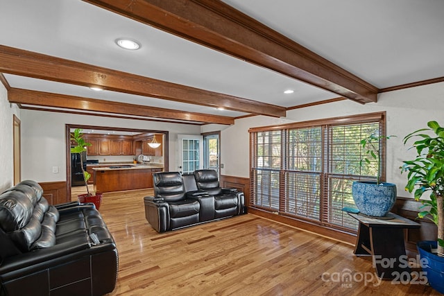 living room with beamed ceiling, light wood-style flooring, wainscoting, and crown molding