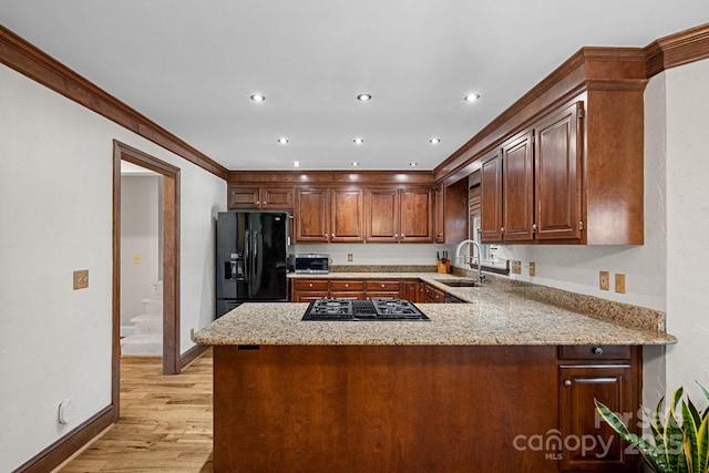 kitchen featuring a sink, light stone countertops, black appliances, and a peninsula