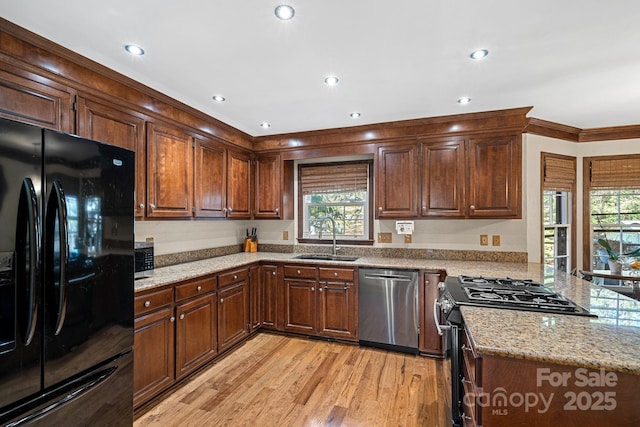 kitchen featuring light stone counters, a peninsula, light wood-style flooring, a sink, and appliances with stainless steel finishes