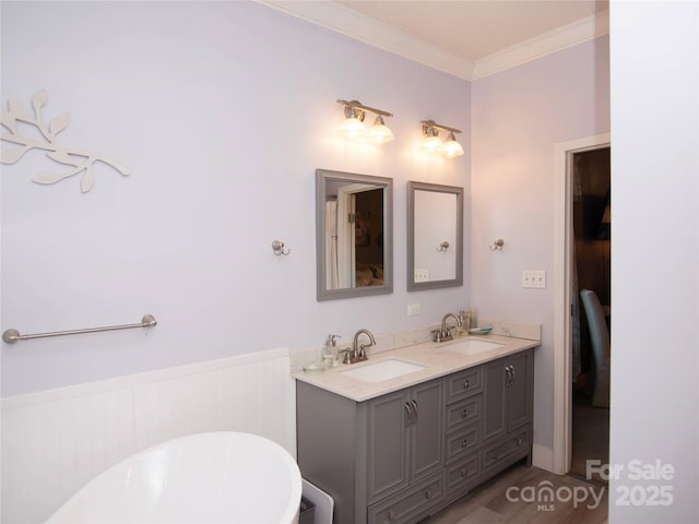 bathroom with a wainscoted wall, a freestanding bath, crown molding, and a sink