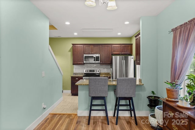 kitchen with backsplash, appliances with stainless steel finishes, a breakfast bar area, a peninsula, and light stone countertops