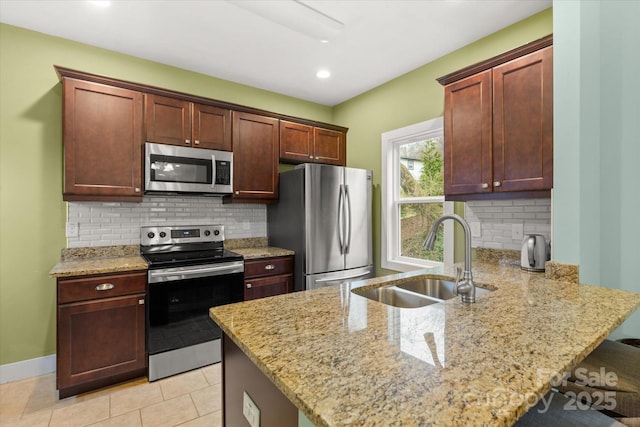 kitchen featuring a breakfast bar area, light stone counters, a peninsula, stainless steel appliances, and a sink