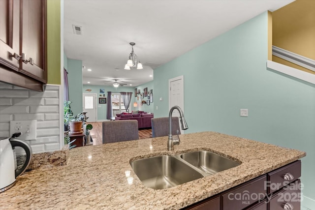 kitchen featuring light stone counters, visible vents, a sink, dark brown cabinets, and pendant lighting