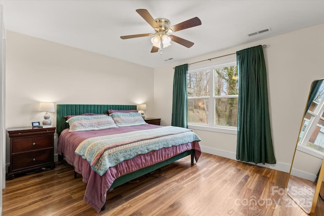 bedroom with a ceiling fan, wood finished floors, visible vents, and baseboards