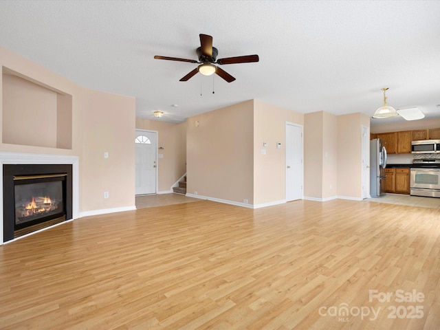 unfurnished living room featuring a glass covered fireplace, stairway, light wood-type flooring, and baseboards