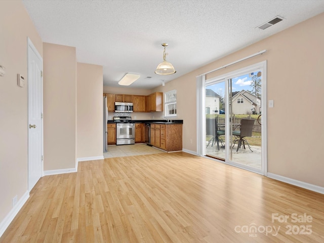 kitchen with brown cabinetry, visible vents, light wood-style floors, appliances with stainless steel finishes, and dark countertops