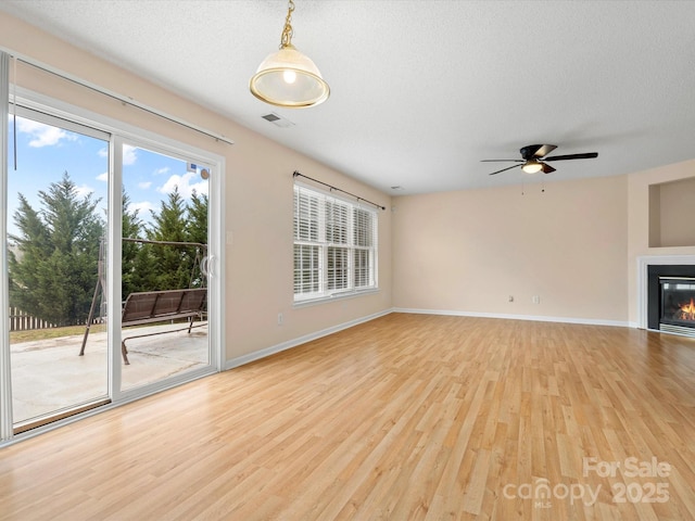 unfurnished living room with visible vents, a textured ceiling, a glass covered fireplace, and light wood finished floors