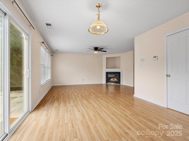 unfurnished living room featuring visible vents, baseboards, light wood-style flooring, a glass covered fireplace, and a ceiling fan