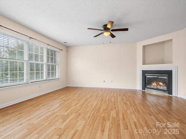 unfurnished living room featuring visible vents, a textured ceiling, a glass covered fireplace, wood finished floors, and baseboards