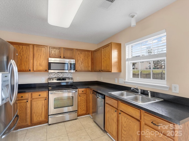 kitchen with brown cabinetry, visible vents, a sink, appliances with stainless steel finishes, and dark countertops