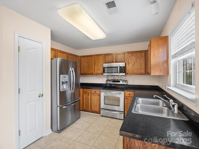 kitchen with dark countertops, visible vents, brown cabinets, appliances with stainless steel finishes, and a sink