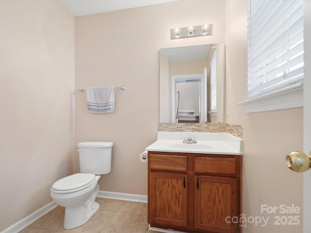 half bathroom with tile patterned floors, toilet, tasteful backsplash, baseboards, and vanity