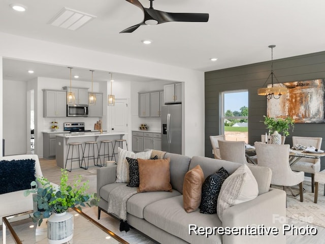 living room featuring recessed lighting, visible vents, wood walls, and ceiling fan with notable chandelier