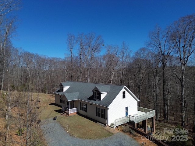 view of front of property with gravel driveway, covered porch, a wooded view, and a shingled roof