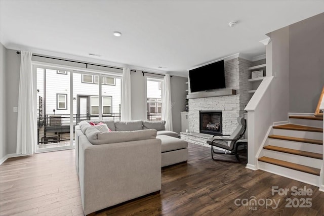 living room with wood finished floors, baseboards, a fireplace, ornamental molding, and stairs