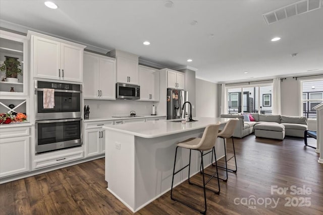 kitchen with visible vents, an island with sink, a sink, white cabinetry, and stainless steel appliances