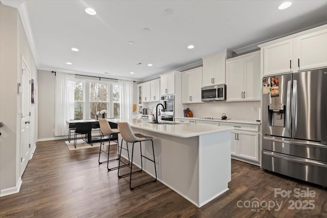 kitchen with a kitchen island with sink, ornamental molding, backsplash, dark wood-style floors, and stainless steel appliances