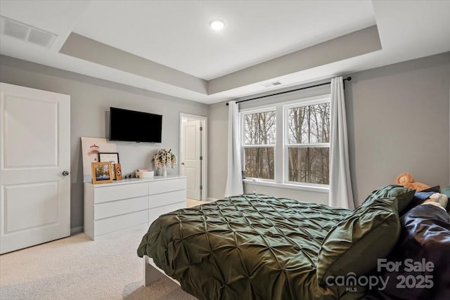 bedroom featuring a tray ceiling, light colored carpet, and visible vents