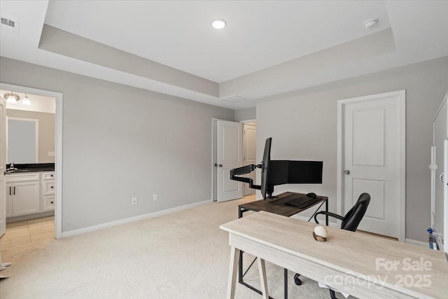 office area featuring light colored carpet, a raised ceiling, and baseboards