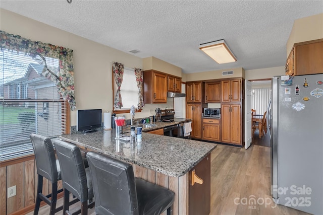 kitchen with visible vents, a peninsula, a sink, stainless steel appliances, and brown cabinets