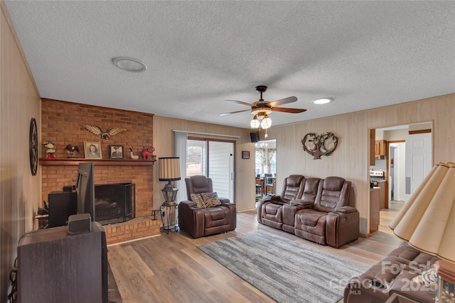 living room featuring a brick fireplace, a textured ceiling, ceiling fan, and wood finished floors