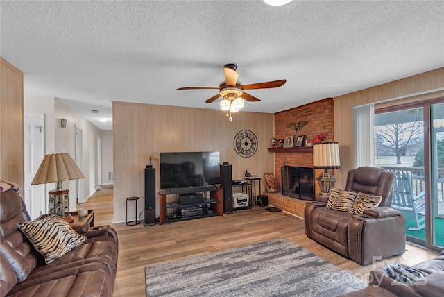 living room with wooden walls, a ceiling fan, light wood finished floors, a fireplace, and a textured ceiling