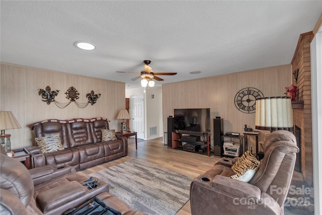 living area featuring visible vents, a textured ceiling, a ceiling fan, and wood finished floors