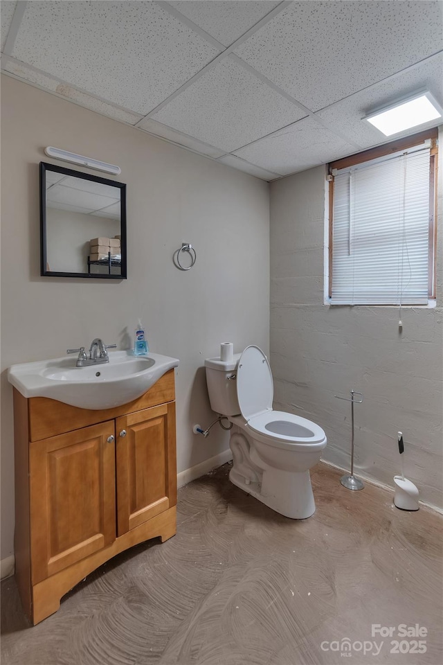 half bath featuring vanity, toilet, a paneled ceiling, and baseboards