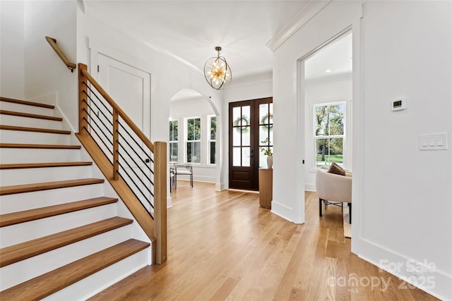 foyer entrance featuring arched walkways, a notable chandelier, light wood-style floors, ornamental molding, and stairs