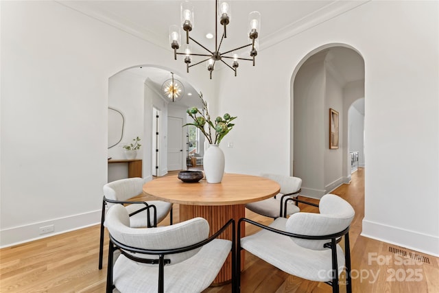 dining space featuring arched walkways, a notable chandelier, visible vents, and light wood-type flooring