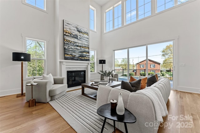 living area featuring a fireplace, baseboards, light wood-style flooring, and a towering ceiling